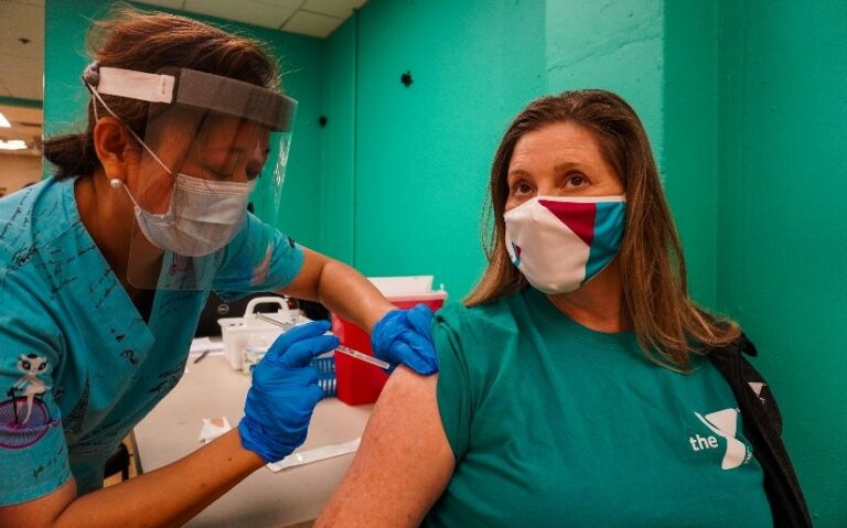 a nurse is giving the Covid-19 vaccine to a person wearing the YMCA tshirt