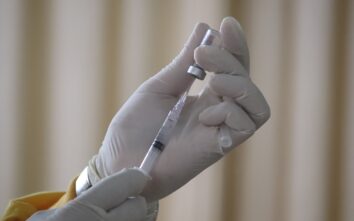 Hands covered with gloves holding a vaccine with the needle
